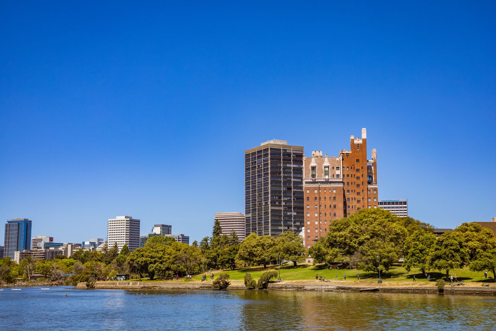 A vibrant city skyline with lush greenery by the waterfront under a blue sky.