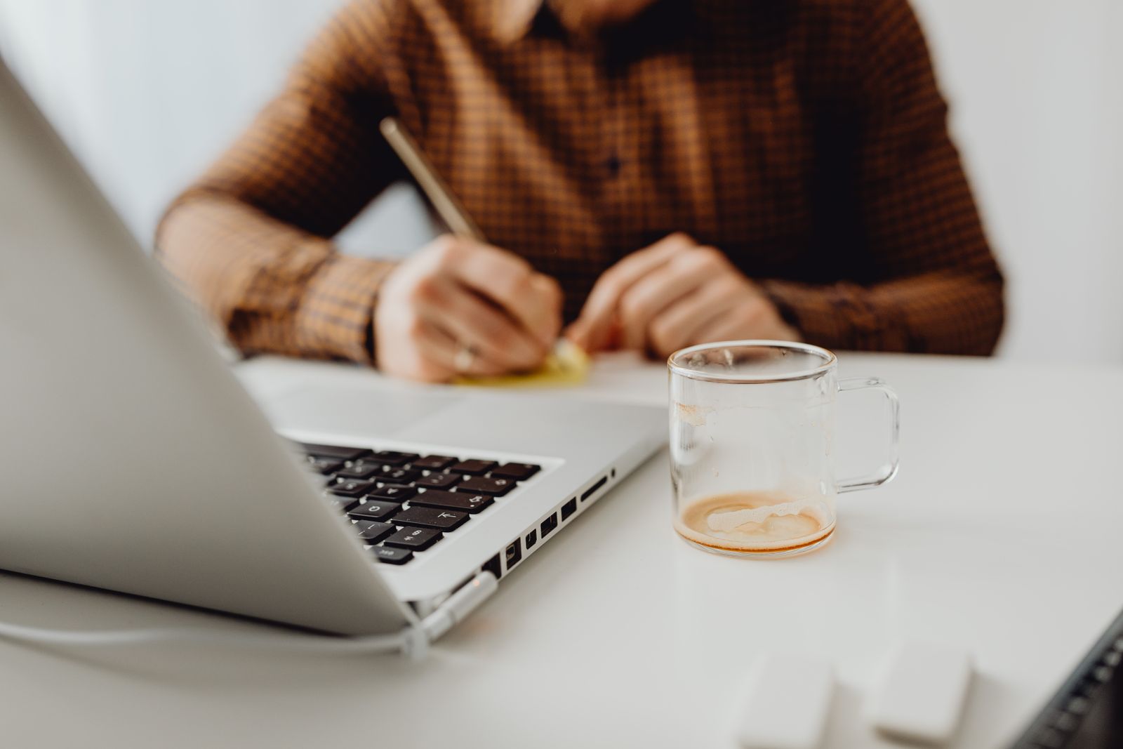 Close-up of a person writing with a notebook and a glass cup on a desk.